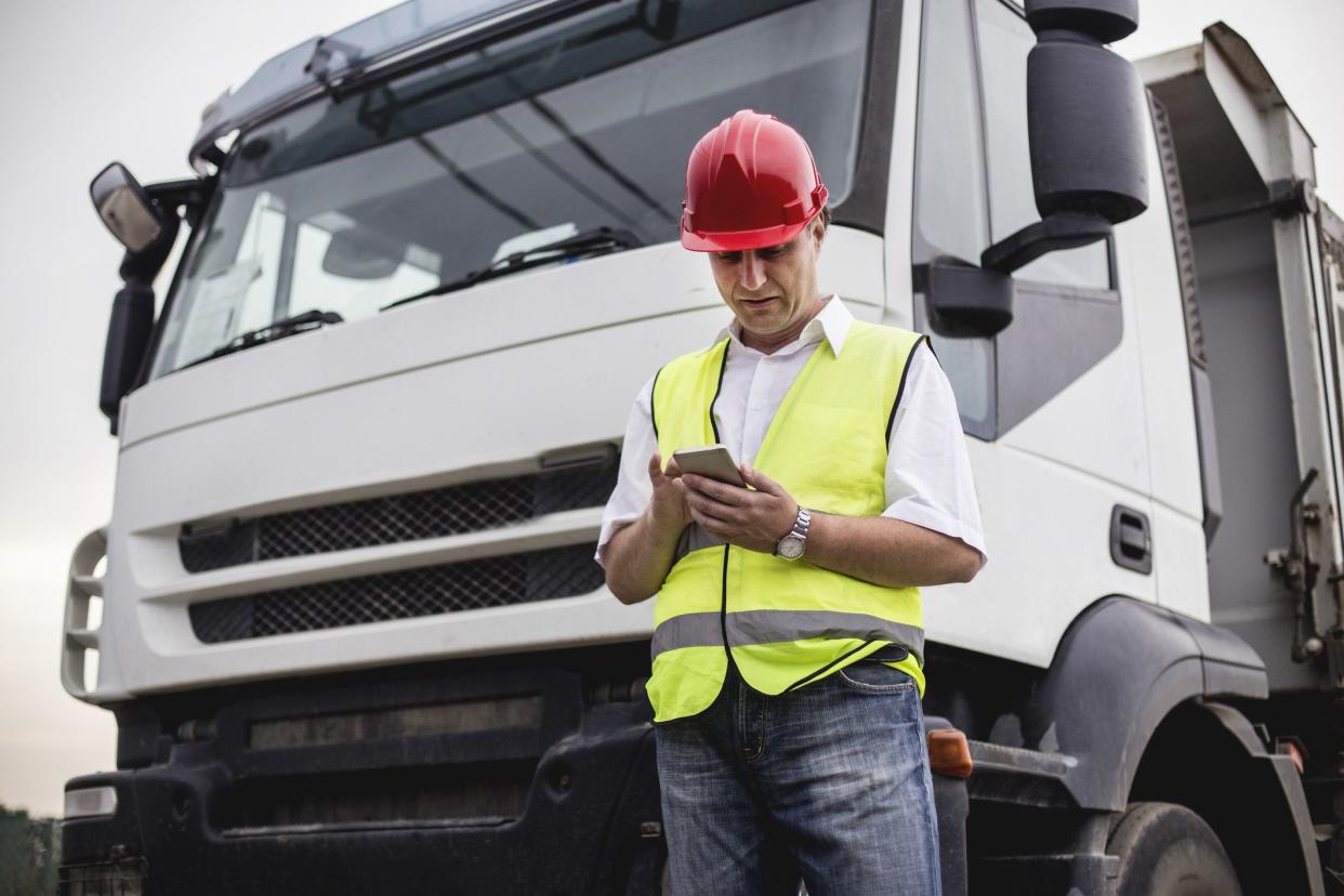truck driver looking at phone standing in front of truck