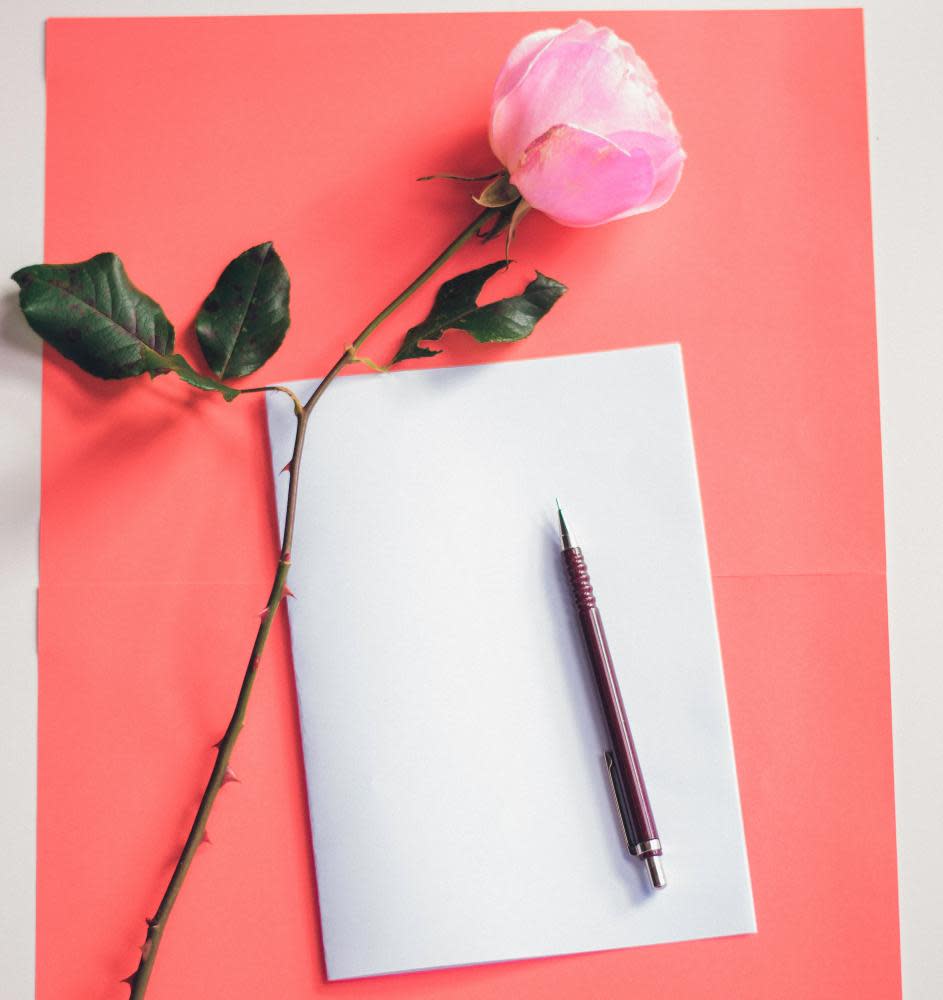 A peen and writing paper with a pink flower on pink background