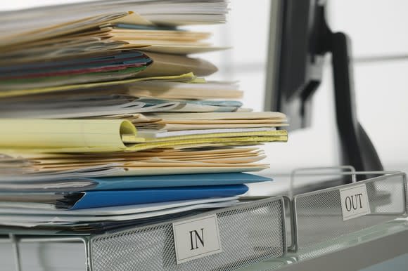 An inbox with a huge stack of files in it next to an empty out box.