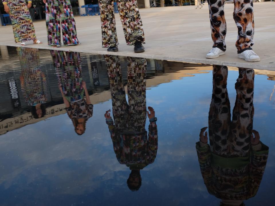 Four people wearing Cap_able's vibrant outfits stand in a line and are reflected in the water