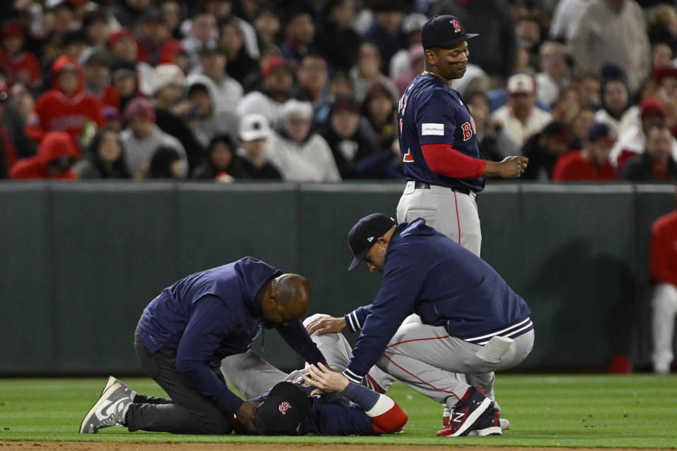 Boston Red Sox shortstop Trevor Story receives attention from a trainer and manager Alex Cora, right, after being injured on a single by Los Angeles Angels' Mike Trout during the fourth inning of a baseball game in Anaheim, Calif., Friday, April 5, 2024. (AP Photo/Alex Gallardo)
