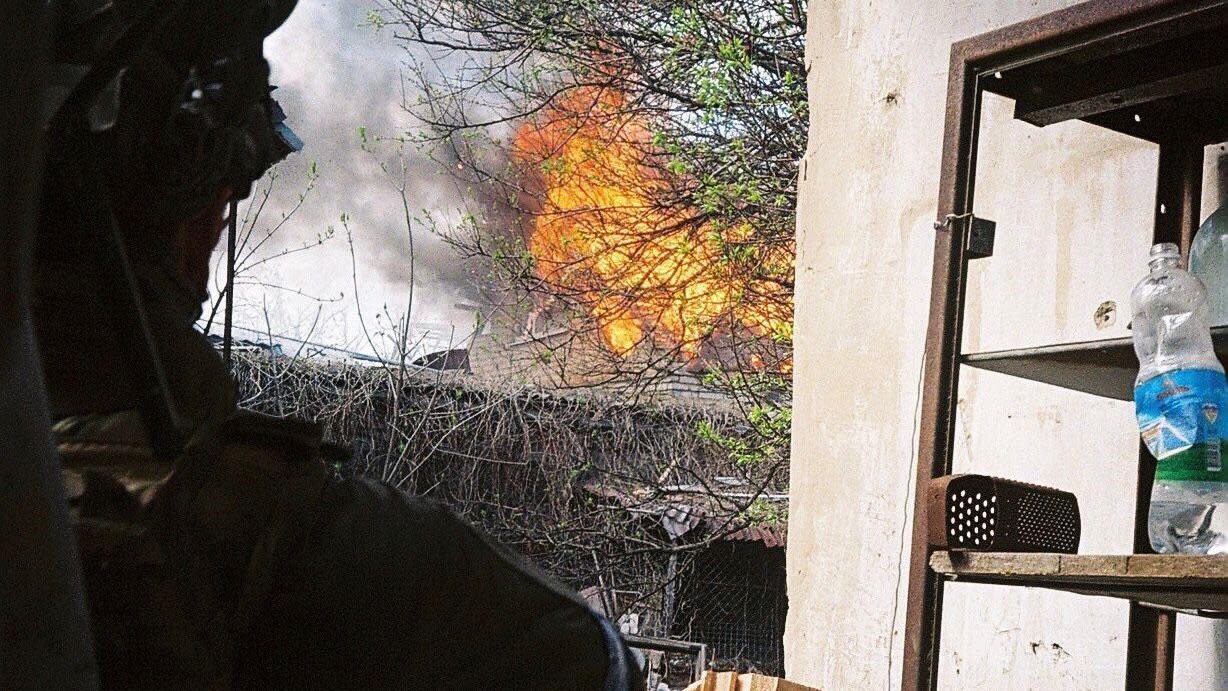 An untrained Ukrainian soldier stands outside, watching a building burn