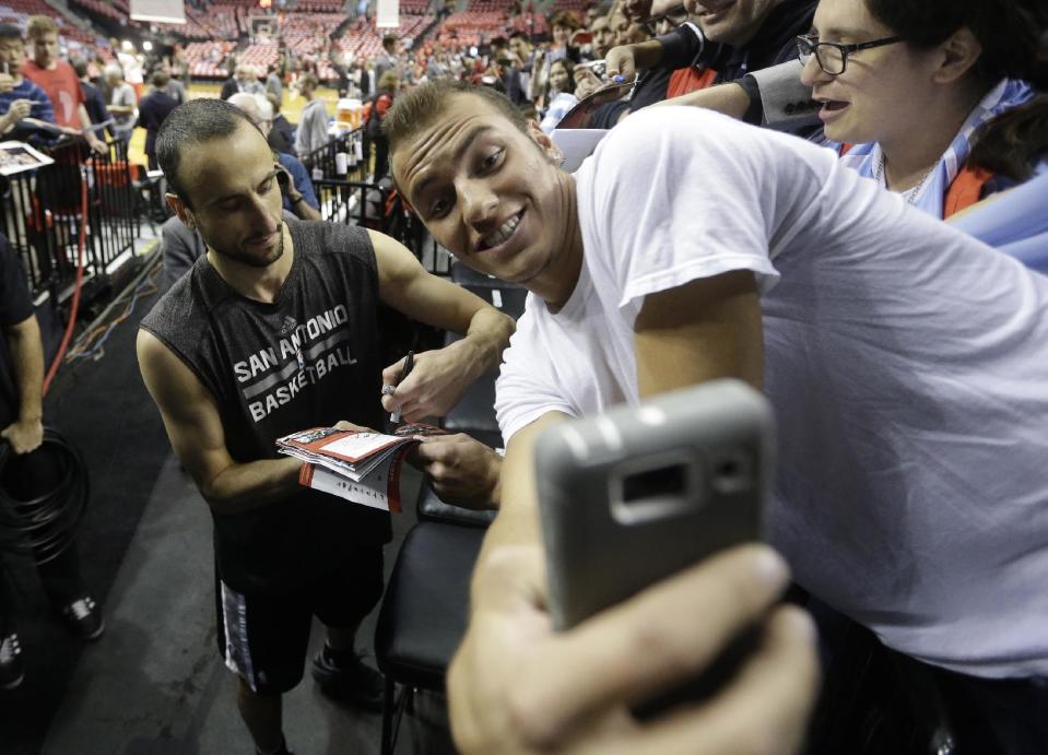 A fan snaps his photo with San Antonio Spurs' Manu Ginobili (20) as he signs autographs after practice before the start of their Game 3 of a Western Conference semifinal NBA basketball playoff series with the Portland Trail Blazers, Saturday, May 10, 2014, in Portland, Ore. (AP Photo/Rick Bowmer)