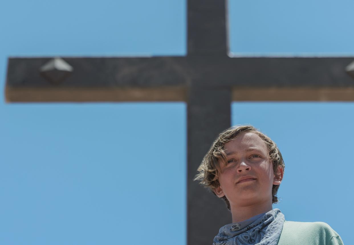 jodie in the chosen one, a preteen boy standing in front of a large cross 