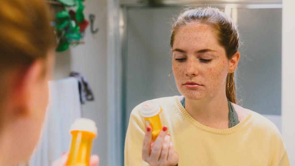 Woman in Bathroom Looking at Pill Bottle.