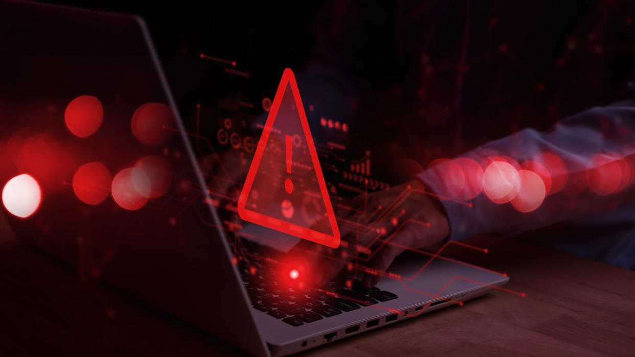  A concept image of someone typing on a computer. A red flashing danger sign is above the keyboard and nymbers and symbols also in glowing red surround it. 