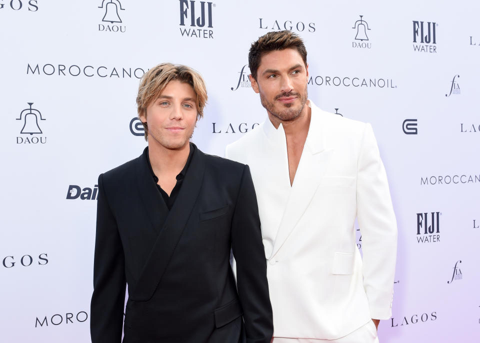 Two men in formal attire posing for a photo; one in a black suit, the other in a white suit