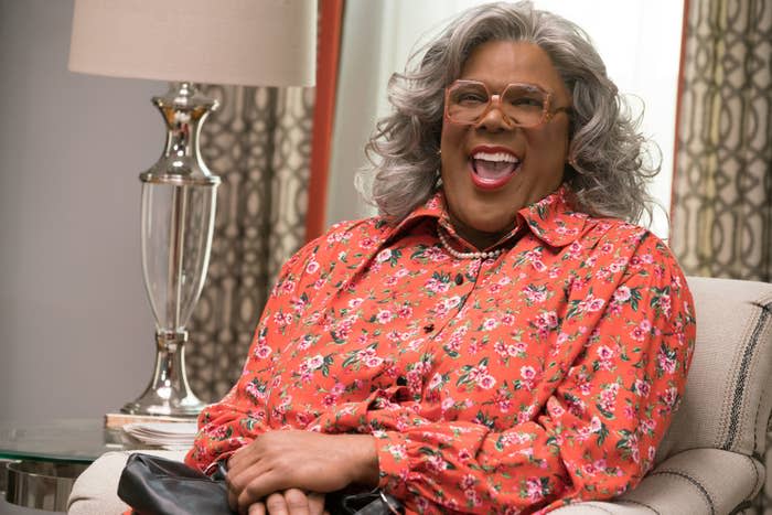 Madea, portrayed by Tyler Perry, sits in a floral blouse, laughing joyfully while sitting on a couch in a well-decorated room