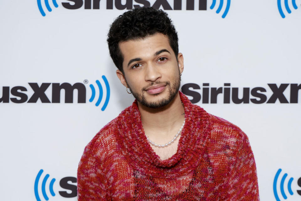 Jordan Fisher poses in a knit sweater in front of a SiriusXM backdrop