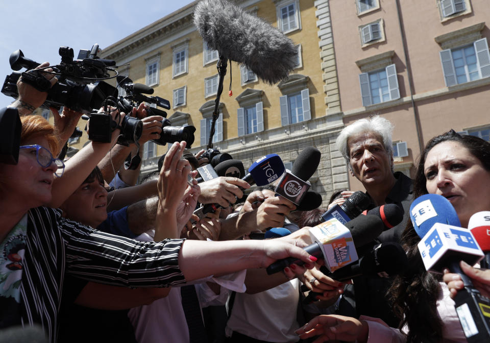 FILE - In this Thursday, July 11, 2019 filer, Pietro Orlandi, brother of Emanuela Orlandi who went missing in 1983, second from right, stands by his lawyer Laura Sgro as she speaks to the media at the Vatican. The mystery over the 1983 disappearance of the 15-year-old daughter of a Vatican employee has taken yet another twist following excavations this week at a Vatican City cemetery. The Vatican said Saturday it had discovered two sets of bones under a stone slab. An official says the area was immediately sealed off and would be opened in the presence of forensic experts on July 20. (AP Photo/Andrew Medichini)