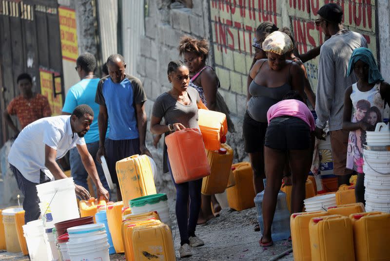Personas esperan en una calle para recoger agua en cubetas y contenedores en Puerto Príncipe