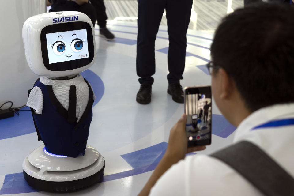 In this July 23, 2019, photo, a man takes photos with his cellphone of a Siasun greeting robot in a demonstration hall of Siasun Robot and Automation in Shenyang in northeastern China's Liaoning Province. From Thailand to Kenya, trains run on tracks from steel mills in China’s northeast, a rust-belt region that is trying to capitalize on a multibillion-dollar national initiative to build ports, railways and other projects abroad. Announced in 2012, the Belt and Road Initiative is helping to boost demand from developing countries at a time when the domestic economy is slowing and exporters face U.S. tariff hikes in a war over trade and technology.(AP Photo/Olivia Zhang)