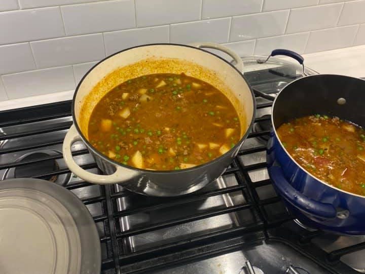 Two pots cooking on a stove with soup inside.