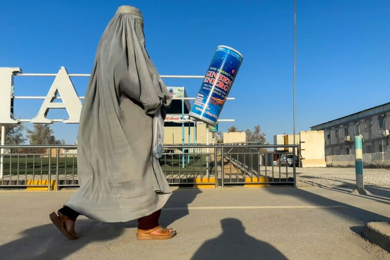 An Afghan burqa-clad woman walks past an energy drink advertisement in Kandahar (Wakil Kohsar)