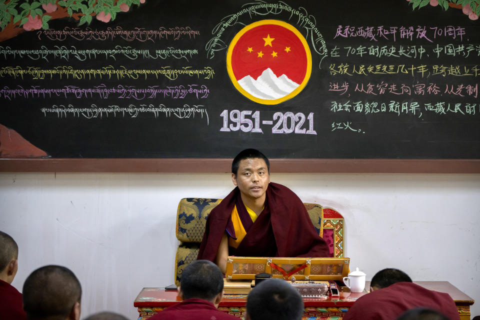 A monk teaches a class while sitting beneath a chalkboard with a mural commemorating the 70th anniversary of the Chinese government's control of Tibet at the Tibetan Buddhist College near Lhasa in western China's Tibet Autonomous Region, Monday, May 31, 2021, as seen during a government organized visit for foreign journalists. High-pressure tactics employed by China's ruling Communist Party appear to be finding success in separating Tibetans from their traditional Buddhist culture and the influence of the Dalai Lama. (AP Photo/Mark Schiefelbein)