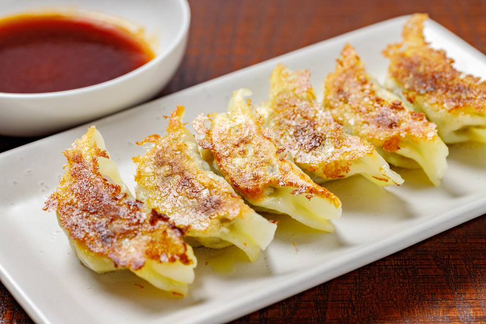 A white plate with gyoza on it and a bowl of dipping sauce