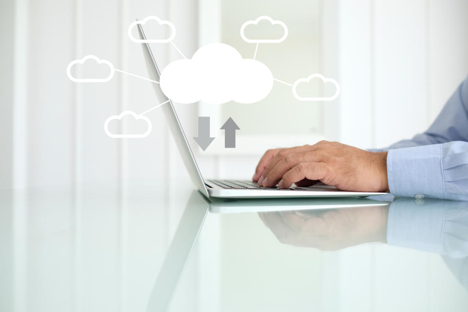 A man's hands typing on a laptop keyboard with white clouds hovering above the computer