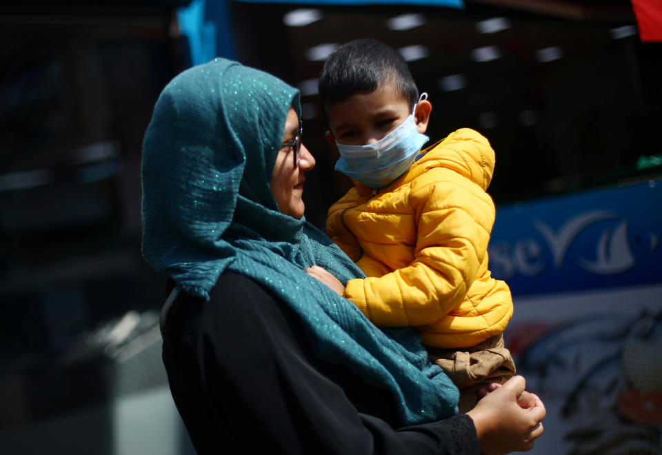 A woman carries a child in her arms who wears a face mask in Tooting, following the outbreak of the coronavirus disease (COVID-19), London, Britain, May 4, 2020. REUTERS/Hannah McKay