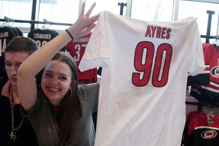 Salesperson Beth Knight shows a shirt for sale with Dave Ayres name and number at the team store before an NHL hockey game between the Carolina Hurricanes and the Dallas Stars in Raleigh, N.C., on Tuesday, Feb. 25, 2020. Ayres became a sudden hero to Hurricanes fans when he came into the game as an emergency goaltender in Toronto on Saturday and won the game. (AP Photo/Chris Seward)