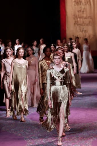 Dior models dressed like Greek goddesses inside artist Judy Chicago's installation, "The Divine Female", with her main banner in the background