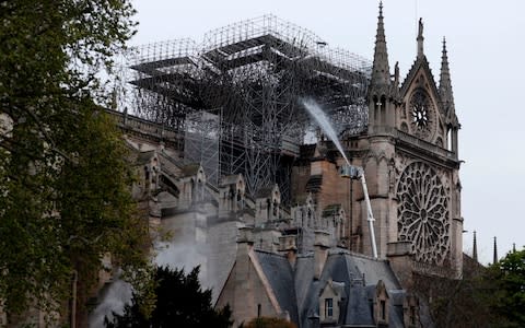 Firefighters spray water as they work to extinguish a fire at Notre-Dame Cathedral in Paris early on Tuesday - Credit: AFP