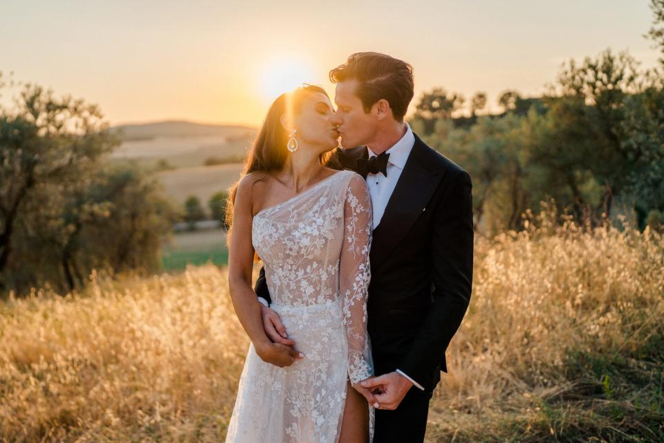 A bride and groom kiss at sunset.