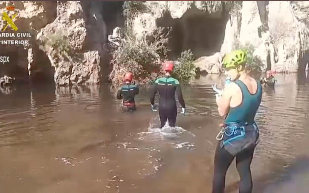 Three people wearing wetsuits search a flooded canyon