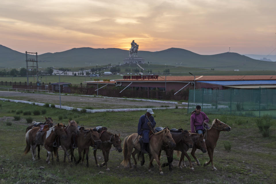 Mongolians herd horses near a 40-meter (130-foot-) tall stainless steel statue of Genghis Khan, a national hero who amassed power to become the leader of the Mongols in the early 13th century, on the outskirts of Ulaanbaatar, Mongolia, Monday, July 1, 2024. (AP Photo/Ng Han Guan)