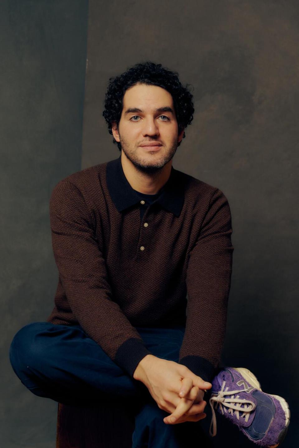 Benny Safdie sits with crossed leg, his foot resting on his knee.