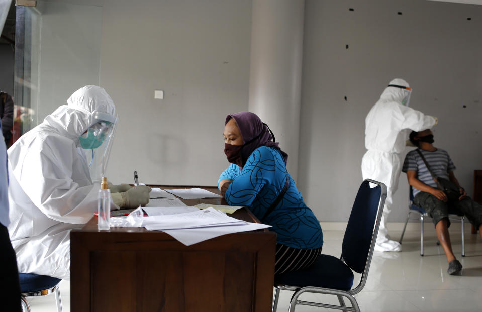 A heath worker checks ID of woman as she waits to takes a nasal swab sample during a public testing for the coronavirus conducted at a market in Bali, Indonesia on Saturday, June 6, 2020. (AP Photo/Firdia Lisnawati)