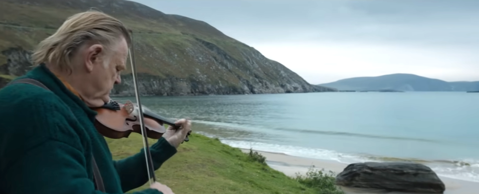 Colm playing the violin outside his house, looking out over the ocean