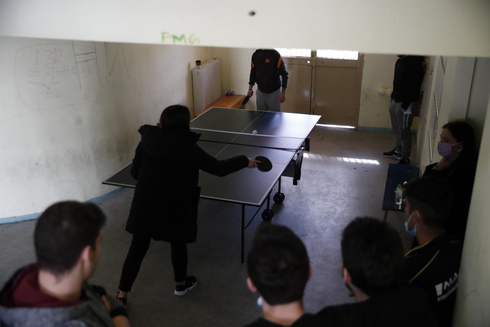 A teacher plays table tennis with an inmate as others watch them at Avlona's prison school, north of Athens, Wednesday, Feb. 10, 2021. With Greece's schools shut due to the pandemic, all lessons have gone online. But the online world isn't within reach of everyone _ and particularly not within reach of the students of Avlona Special Youth Detention Center, where internet devices are banned by law from the cells. (AP Photo/Thanassis Stavrakis)