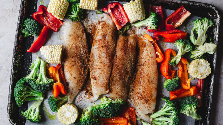 raw fish, broccoli, pepper slices and corn cobs on sheet pan