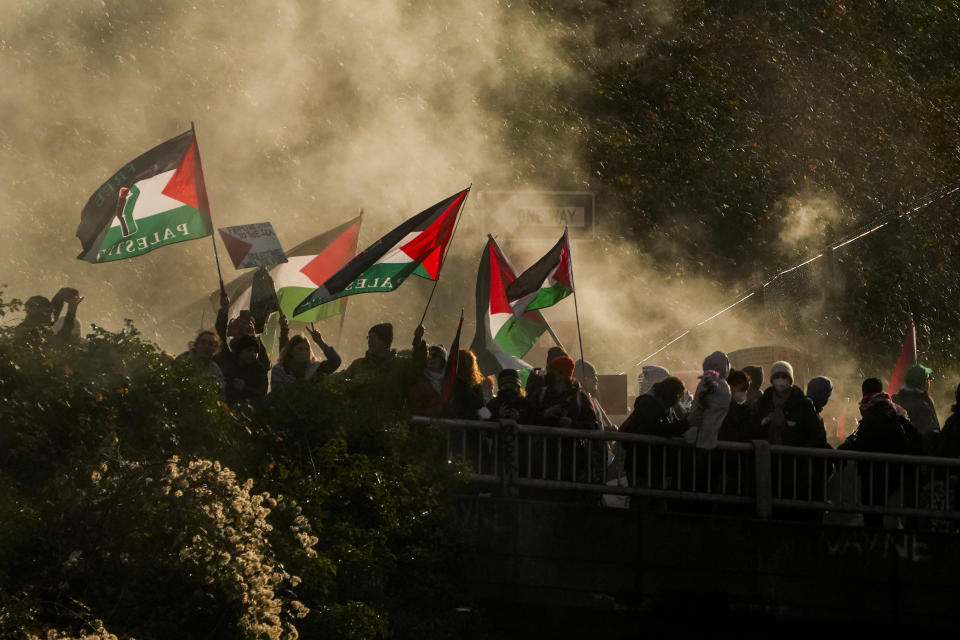 Protesters calling for a cease-fire in the Israel-Hamas war wave flags through smoke from a flare on an overpass as others block Interstate 5 northbound, Saturday, Jan. 6, 2024 in downtown Seattle. (AP Photo/Lindsey Wasson)