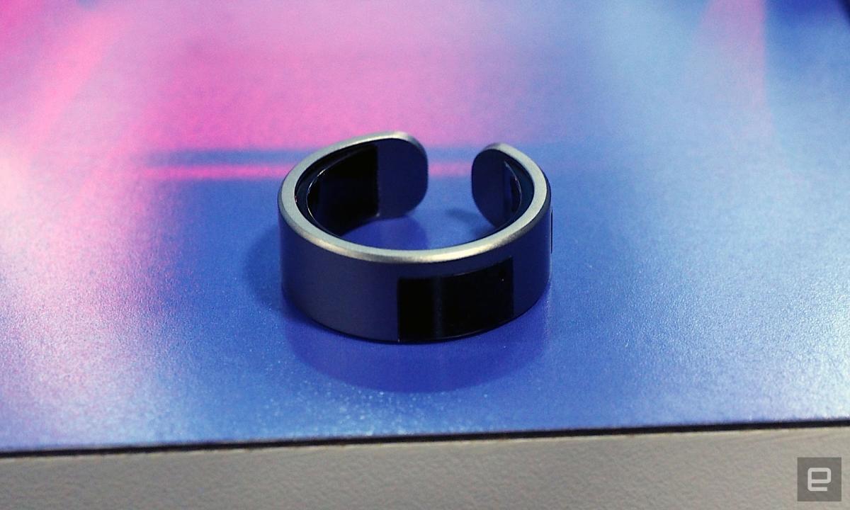 Image of the VTouch Whsp Ring, in dark grey, sat on a blue to pink ombre table.