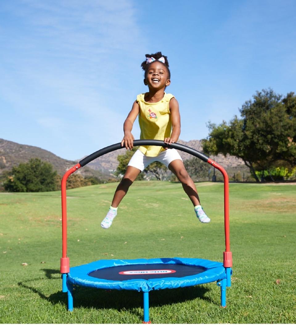 Child jumps on outdoor trampoline with handlebar in a sunny grassy area