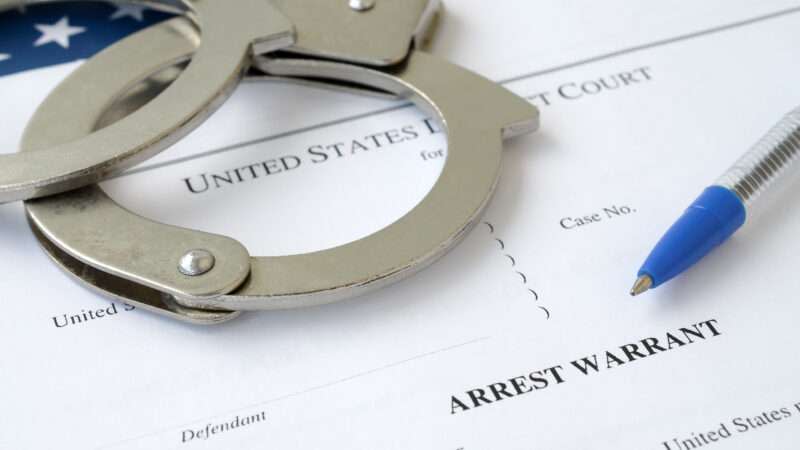 Handcuffs and a ballpoint pen on an arrest warrant.