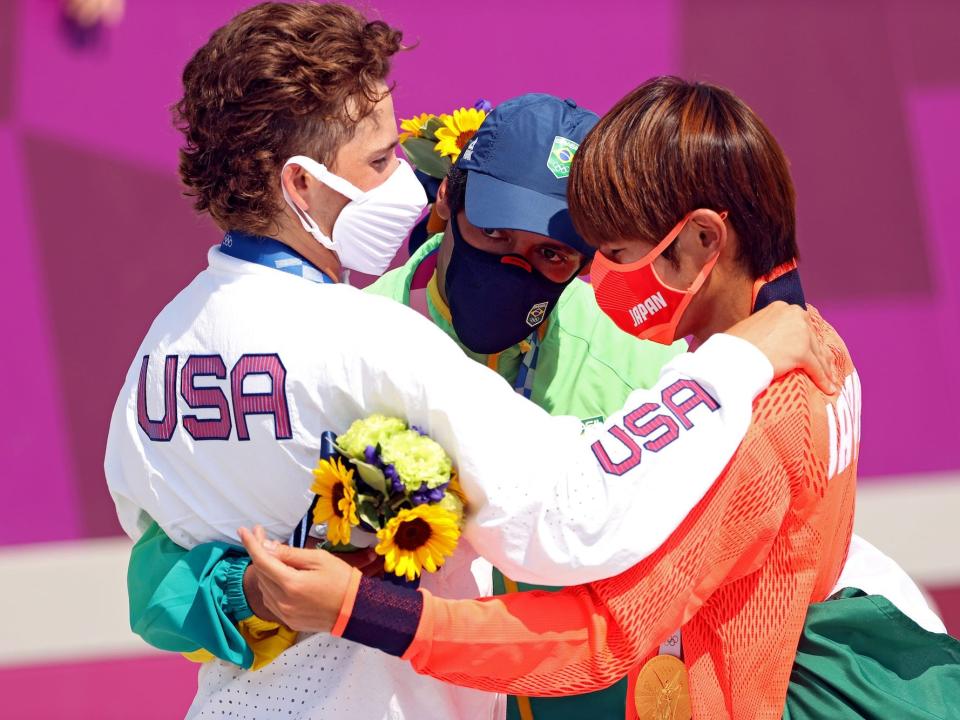 Three medalists in men's street skateboarding hug.