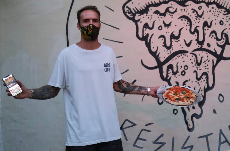 Funky Pizza restaurant owner Carlos Manich poses as he holds his mobile phone with the "Funky Pay" app in one hand and a pizza in the other, at Funky Pizza restaurant, where the app replaces waiters, in Palafrugell