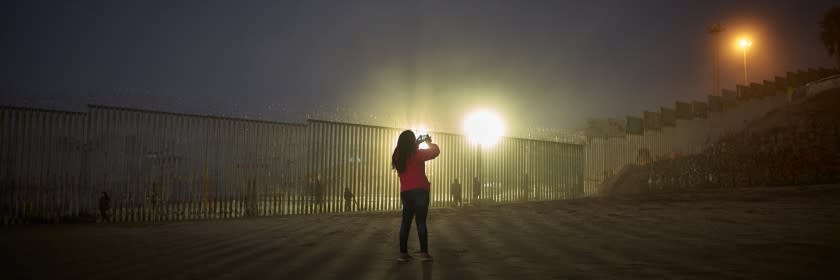 FILE - In this Jan. 10, 2019, file photo, a woman records with her phone, as floodlights from the United States light up the border wall, topped with razor wire along the beach in Tijuana, Mexico. The government is working on replacing and adding fencing in various locations, and Trump in February declared a national emergency to get more funding for the wall. (AP Photo/Gregory Bull, File)