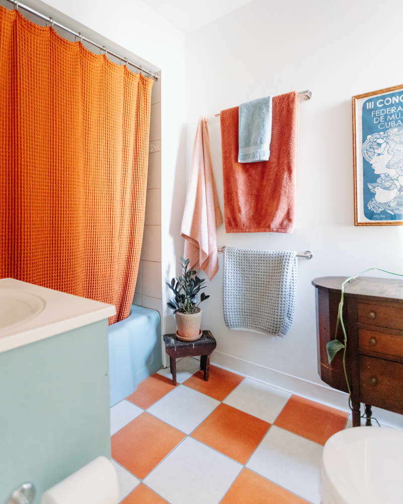 white bathroom with orange and white floor, pale blue tub, and orange shower curtain after makeover