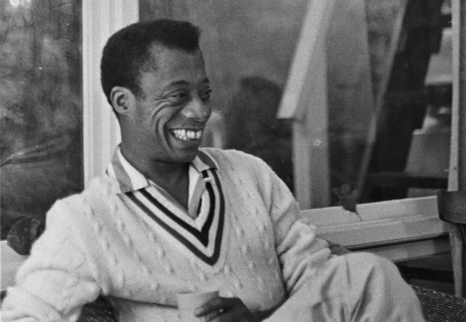 James Baldwin smiling while relaxing on a porch