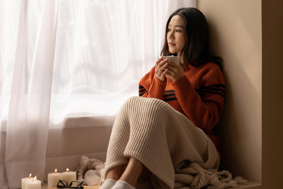 An Asian woman wearing a sweater inhaled the scent and drank the winter morning coffee. She looked at the view from the large window on vacation.