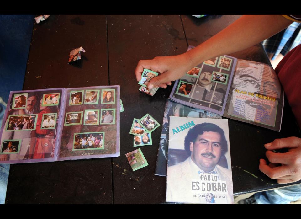 A youth holds baseball card style photographs showing the life of the late Colombian drug trafficker Pablo Escobar the he bought to fill the magazine style publication bellow at a small food store in the neighborhood Comuna Nororiental 1 in Medellin, Colombia, Wednesday, Aug. 8, 2012. The magazine, whose publisher is unknown, comes with blank pages with instructions to fill them with small photographs which are bought separately at several small stores in this neighborhood. The cards showing images of Escobar, are a mix of real life photos and of actors playing out his life from a local TV series called "Escobar, El Patrón del Mal." (AP Photo/Luis Benavides)