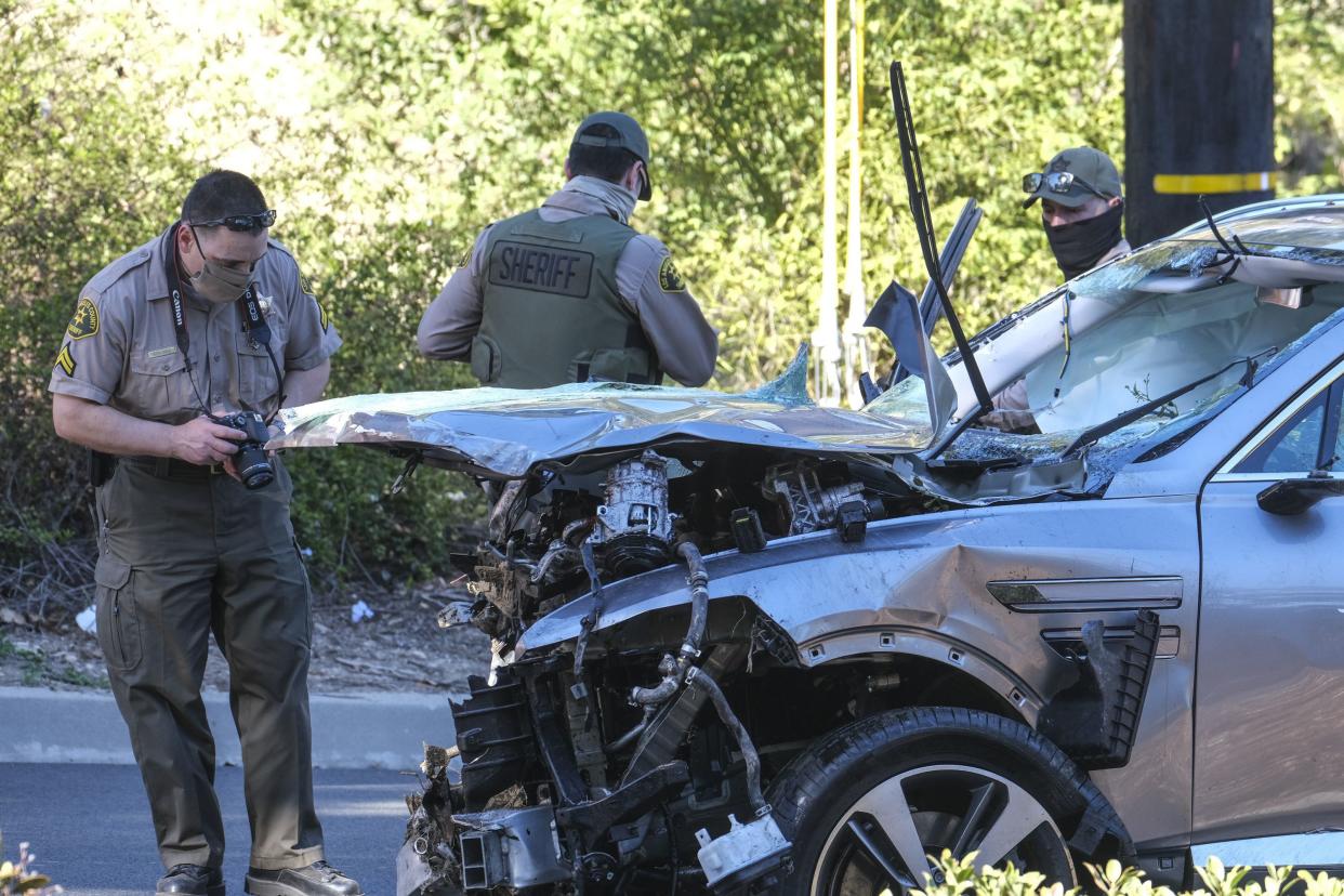 Law enforcement officers look over a damaged vehicle following a rollover accident involving golfer Tiger Woods, Tuesday, Feb. 23, 2021, in the Rancho Palos Verdes suburb of Los Angeles.