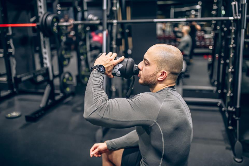 muscular men drink his nutritional supplement in gym