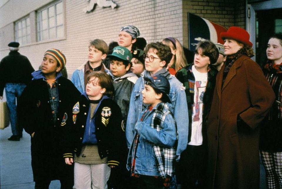 A woman in a red hat stands with a group of children outside a school