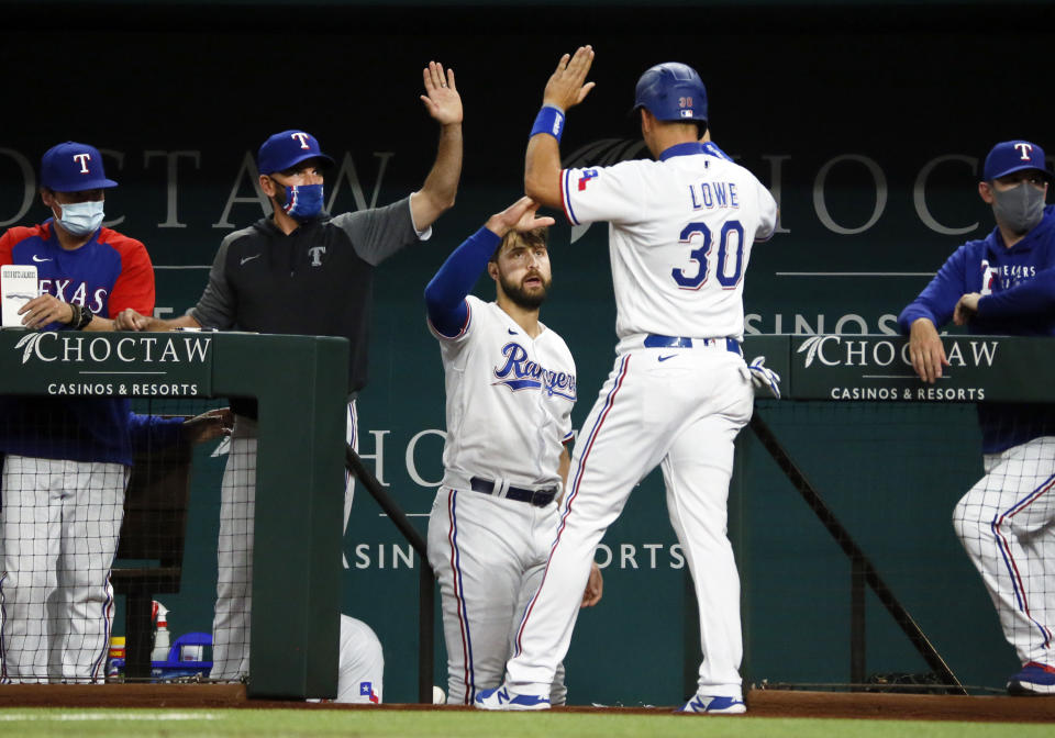 Texas Rangers' Nate Lowe, right, is greeted at the dugout by manager Chris Woodward, left, and Joey Gallo, center, after scoring against the Baltimore Orioles during the fourth inning of a baseball game in Arlington, Texas, Saturday, April 17, 2021. (AP Photo/Ray Carlin)