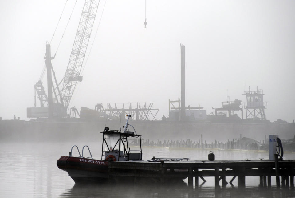 A salvage crane shrouded in fog rises above a barge in a creek near the Tennessee River at the scene of a fatal marina fire at Scottsboro, Ala., on Tuesday, Jan. 28, 2020. Crews already have removed at least two boats that burned at Jackson County Park Marina, and authorities say it could take several days to recover all 35 of the boats that burned in the blaze. (AP Photo/Jay Reeves)