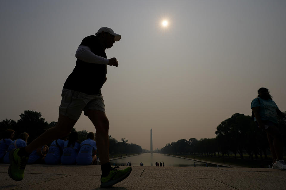 A jogger trots under haze blanketing over the Reflecting Pool with the Washington Monument seen at a distance, Wednesday, June 7, 2023, in Washington. (AP Photo/Julio Cortez)